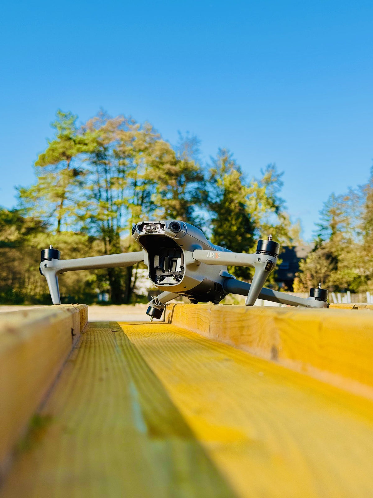 DJI Air 3 mit beschädigtem Gimbal auf einem Holzbalken unter blauem Himmel vor der Reparatur bei CopterTec.
