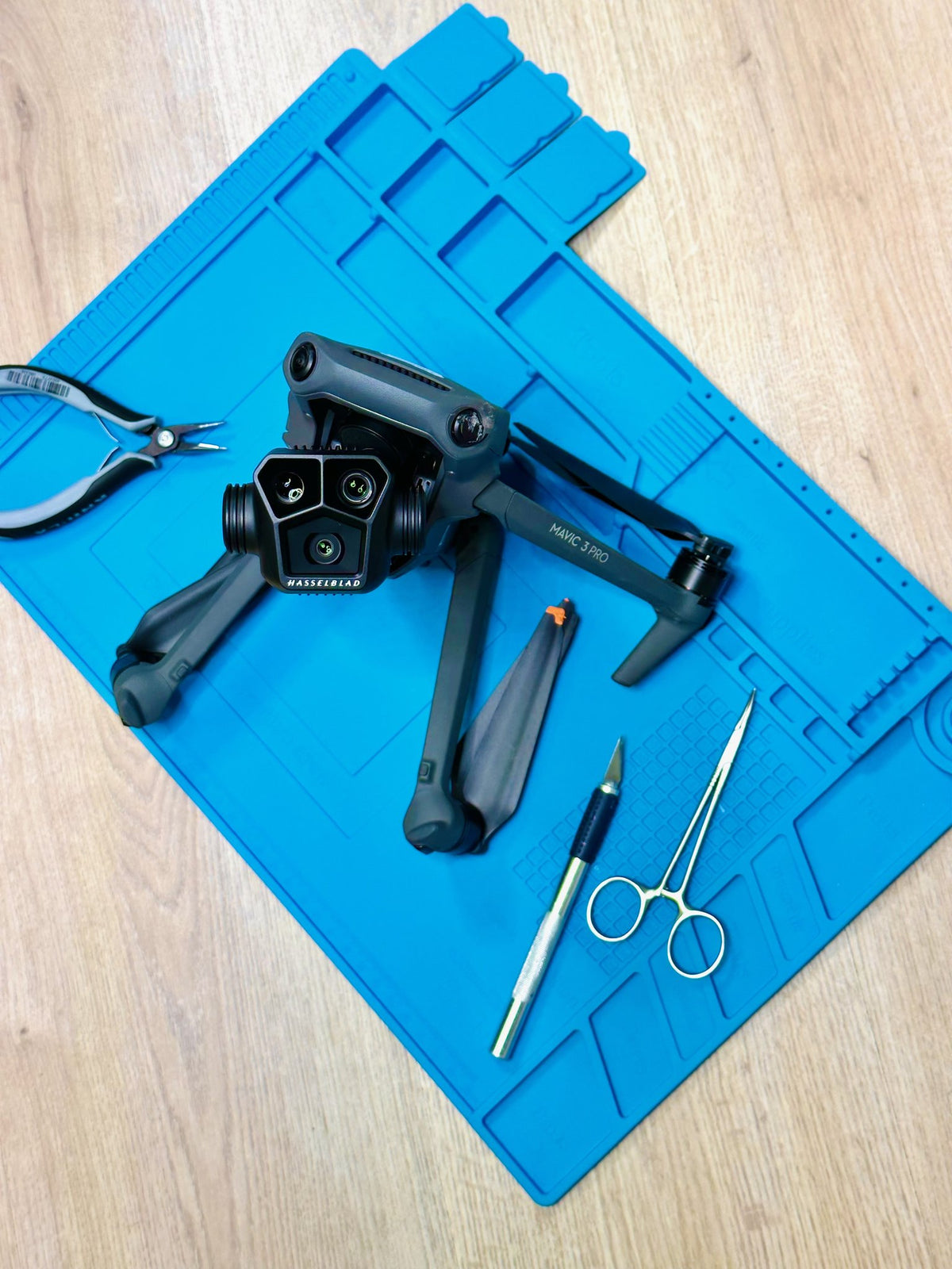 Zerlegter Rahmen einer DJI Mavic 3 Pro mit Gimbal-Kamera und Werkzeug auf der Reparaturmatte bei CopterTec.