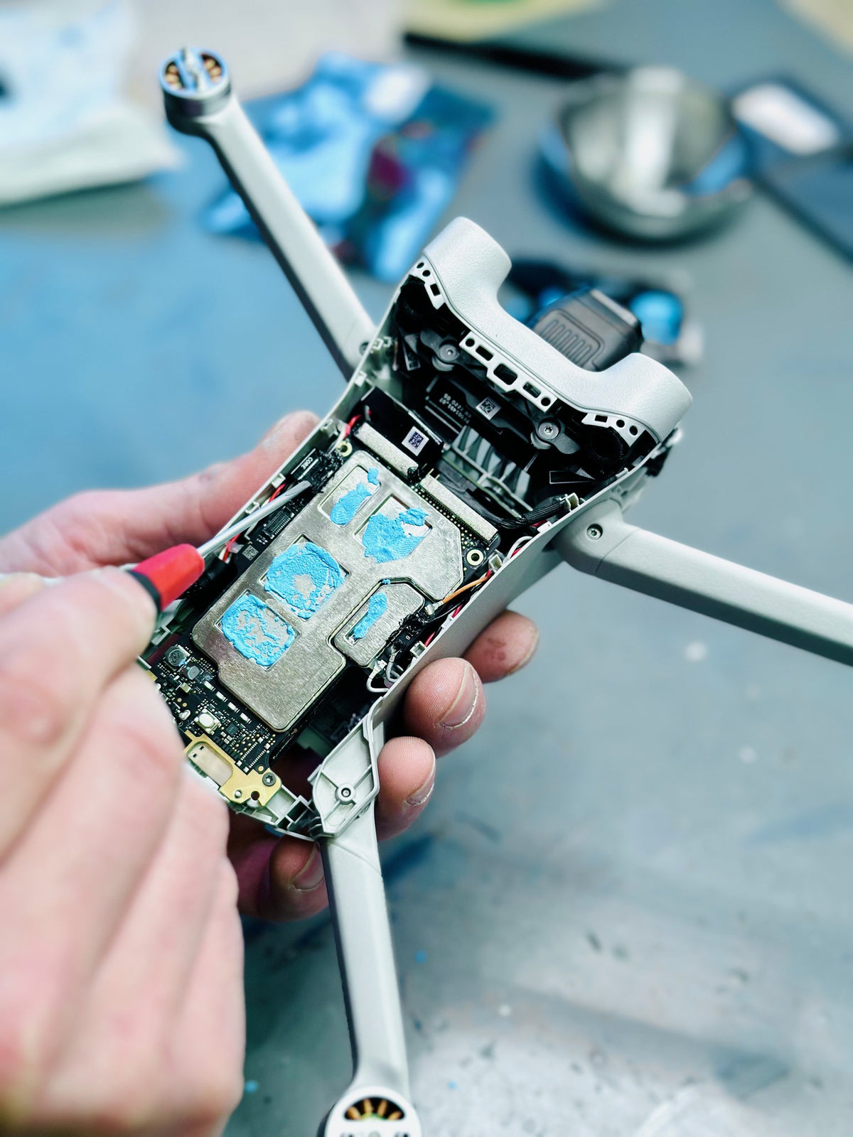 DJI Mini 3 Pro mit freigelegter Platine und frischer Wärmeleitpaste bei der Reparatur in der Hand eines CopterTec-Technikers.