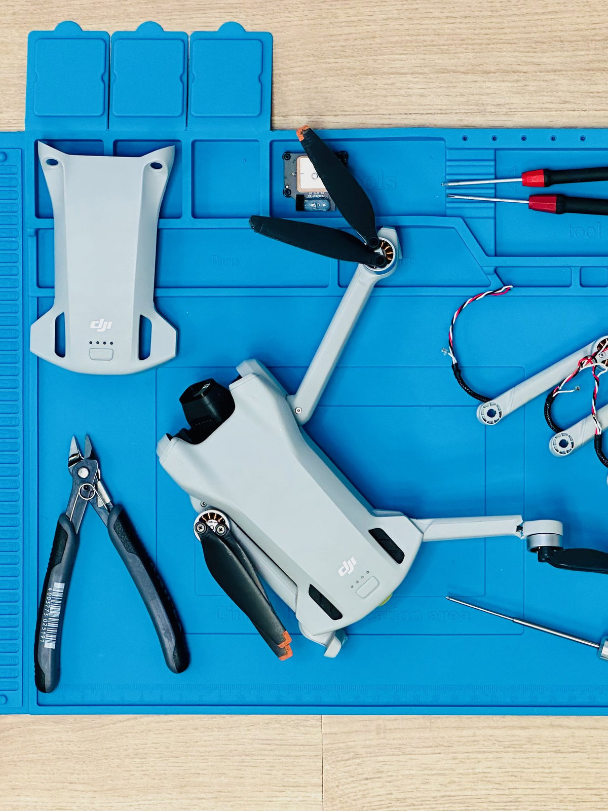 Zerlegte DJI Mini 3 mit Ersatzarmen und Präzisionswerkzeug auf der Reparaturmatte bei CopterTec.
